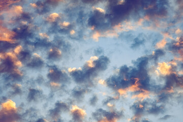 Fototapeta na wymiar Scattered clouds colored in sunset colors moving across a bright blue sky