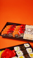 Close up of appetizing sushi in containers on orange background. Set of tasty sushi rolls with different ingredients.