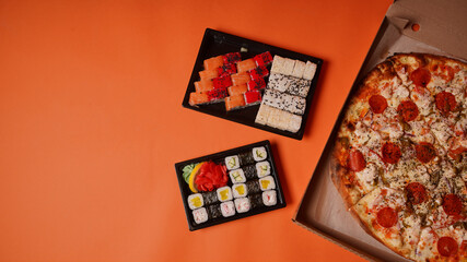 Close up of appetizing sushi in containers and large pizza in box on orange background. Pizza and set of tasty sushi rolls with different ingredients.