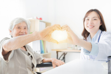 Obraz premium asian female doctor and old patient show heart sign with hand, happiness and relationship in hospital, they feeling happy and smile ,happiness hospital, light and blur people,