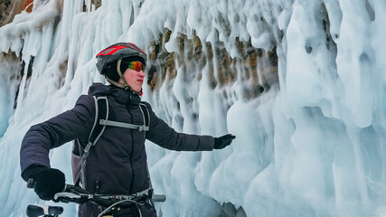 Man is riding bicycle near ice grotto. Rock with ice caves icicles. Teenage is dressed in black...