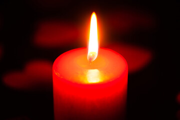 red burning candle on a black background, scattered around red hearts