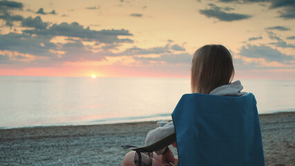 Fototapeta premium Close-up shot of Young woman drinking from thermos and sitting on camping chairs on the beach.