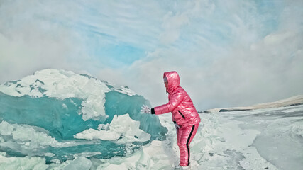 Girl walking on cracked ice of frozen lake Baikal. Woman traveler explores and looks at an ice floe. Magic purest place in nature. Ice arounds traveler all his trip. Hiker walk in cosmic pink jacket. - obrazy, fototapety, plakaty