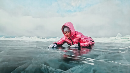Fototapeta na wymiar Girl walking on cracked ice of frozen lake Baikal. Woman traveler explores and looks at an ice floe. Magic purest place in nature. Ice arounds traveler all his trip. Hiker walk in cosmic pink jacket.