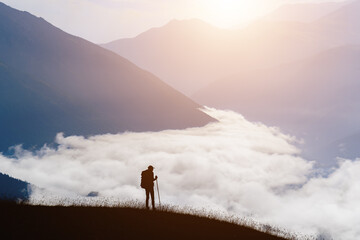 Silhouette of a man traveler in the mountains early in the morning at sunrise. The valley is filled with clouds