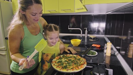 Mother teaching daughter smart girl learning to cook. Young mistress children to cook a Neapolitan egg fried omelette from salame affumicato sausage. Modern Built In Kitchen Appliances.
