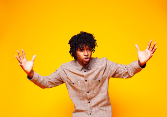 young handsome african american guy student posing cheerful and gesturing on yellow background, lifestyle people concept