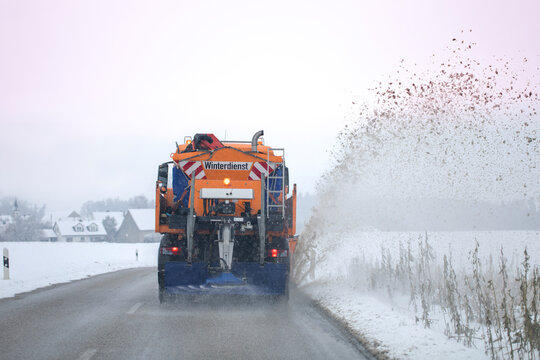 snow plow, winter service on a wet road, winter service truck driving on asphalt road at day while salting the asphalt to protect for freezing