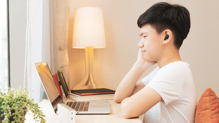 A handsome asian teenager boy with wireless earbuds having good time with online classroom through...