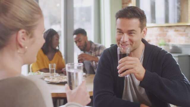 Smiling young couple on date making a toast with soft drinks before enjoying pizza in restaurant together - shot in slow motion