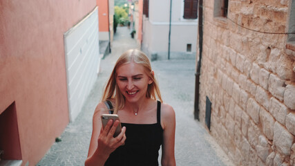 Pretty blonde woman sharing her impressions from summer trip on video call on smartphone while walking the city of her visit