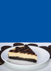 cookies and cream cheesecake on a white plate and stacked cookies on white surface and blue background in portrait. copy space for national cookie day or for advertising.