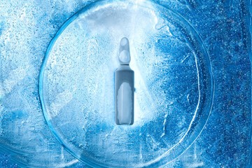 glass frozen ampoule with a virus vaccine on the texture of cold ice top view, background with...