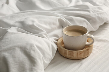 Cup of aromatic coffee on bed with soft blanket, closeup. Space for text