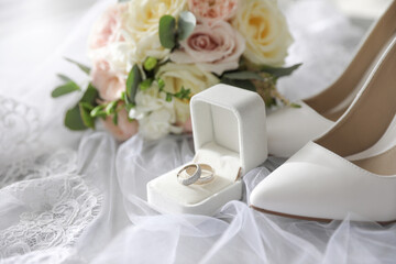 Pair of white high heel shoes, rings and wedding bouquet on lace veil
