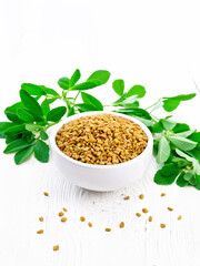 Fenugreek with green leaves in bowl on light wooden board