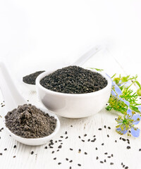 Seeds of black cumin in bowl on light wooden board