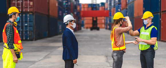 Professional of group cargo foreman in helmets standing and using infrared thermometer for checking body temperature staff fever before work in quarantine for coronavirus wearing protective mask