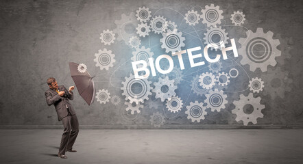 Businessman defending with umbrella from BIOTECH inscription, technology concept