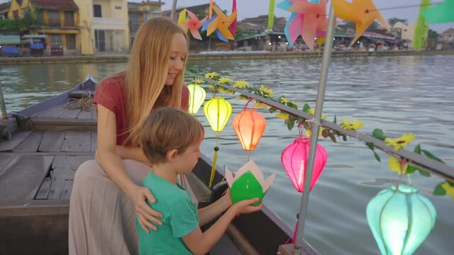 A young woman and her son tourists visit an ancient town of Hoi An in the central part of Vietnam. They are taking a ride on a boat decorated with glowing colourful lanterns. Travel to Vietnam concept