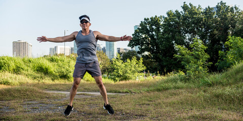 An athletic asian guy does jumping jacks at a open field near the city. Cardiovascular fitness. Working out outdoors.