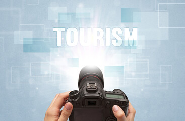Close-up of a hand holding digital camera with TOURISM inscription, traveling concept