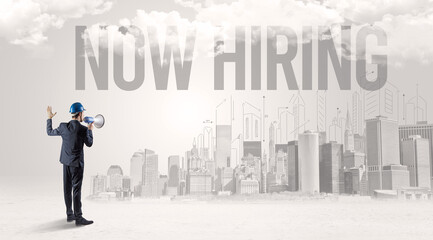 Fototapeta premium Young businessman with hard hat and NOW HIRING inscription, new business opportunity concept