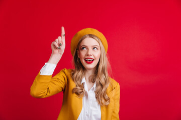 Curious french woman pointing with finger up. Studio shot of refined stylish girl in yellow beret.