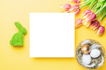 Naklejka na ściany i meble Easter set. Golden, white colour egg in basket with spring tulips, feathers on pastel yellow background in Happy Easter decoration. Traditional design with copy space.