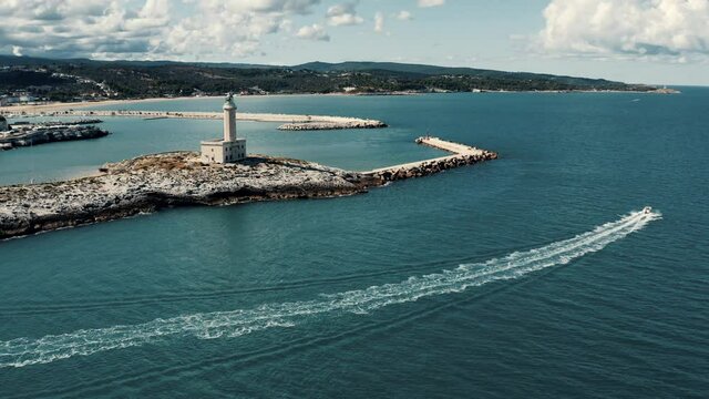 Aerial view on lighthouse on a small island in Italy with boat riding nearby.