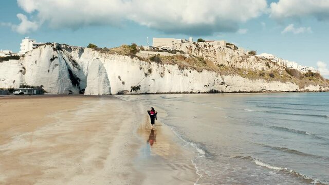 Girl is walking on the beach with rocks in the background.