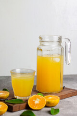 Es jeruk peras or orange juice iced with cut of sweet oranges. Served on clear glass on wooden rustic board. Grey grainy background. 