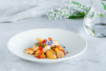 Scallops, potatoes, red caviar, fresh flowers decor in round plate