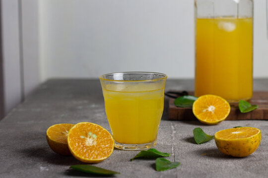 Es jeruk peras or orange juice iced with cut of sweet oranges. Served on clear glass on wooden rustic board. Grey grainy background. 