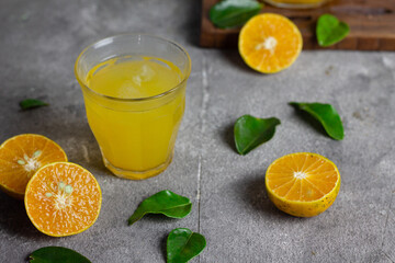 Es jeruk peras or orange juice iced with cut of sweet oranges. Served on clear glass on wooden rustic board. Grey grainy background. 