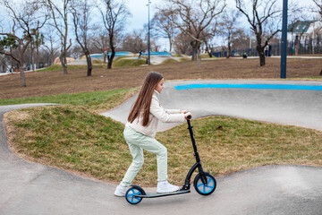 Preteen girl scooter scatii    g in the park after school in the rollerdome. Rest time for the child after school