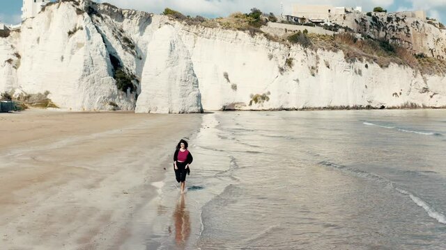 Girl is running on the beach with rocks in the background.