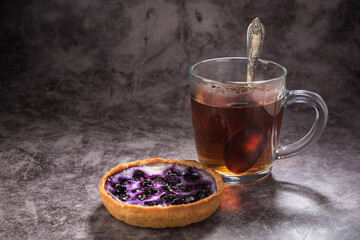 Tea in a glass cup with a spoon, blueberry cake on a gray background