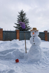 Obraz premium A snowman in a straw hat and with a carrot nose in the winter garden, holding a broom in his 