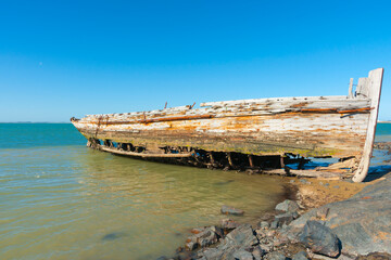 Fototapeta na wymiar Rotting holed hulk of old wooden fishing boat beached