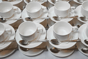 A group of empty white cups and saucers with a teaspoon. Many rows of white cups of tea for serving for breakfast or buffet at the seminar.