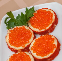 Sandwiches with red caviar and sprigs of parsley close up on a white plate on a tablecloth background