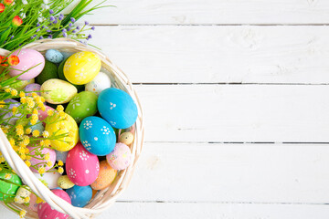 Colored easter eggs in the basket and spring flowers on wooden background. Greeting card - 409377788