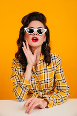Interested pinup girl posing in elegant sunglasses. Studio shot of charming brown-haired lady in...