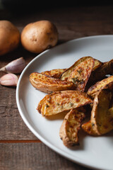 Delicious baked country potatoes in a large white plate with spices, dill and green onions, on a wooden table