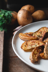 Delicious baked country potatoes in a large white plate with spices, dill and green onions, on a wooden table