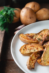 Delicious baked country potatoes in a large white plate with spices, dill and green onions, on a wooden table