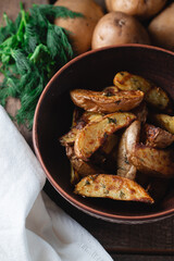 Delicious baked country potatoes in a earthen bowl with spices, dill and green onions, on a wooden table