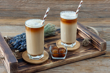 Latte or cappuccino with milk foam and lavender in a tall glass on wooden tray